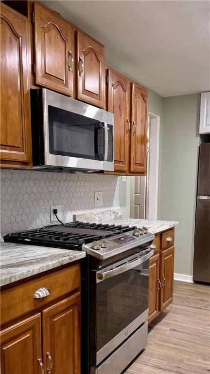 kitchen featuring light stone counters, backsplash, light hardwood / wood-style floors, and appliances with stainless steel finishes