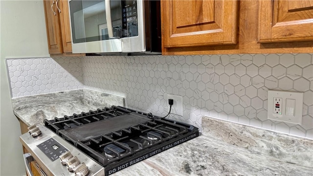 kitchen with stainless steel appliances, light stone countertops, and backsplash