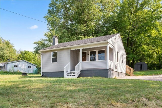 view of front of property featuring covered porch, a storage unit, and a front yard