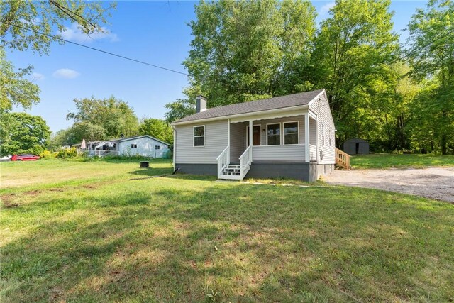 view of front of home with a porch, a shed, and a front lawn