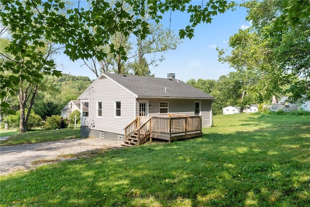 rear view of house with a shingled roof, a lawn, a wooden deck, a chimney, and gravel driveway