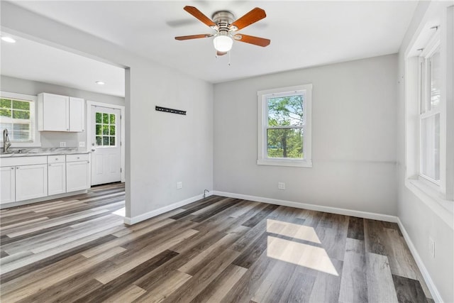 empty room featuring a sink, wood finished floors, a ceiling fan, and baseboards