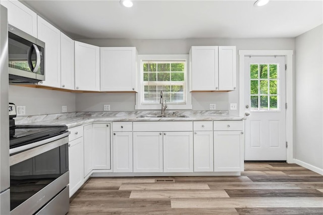 kitchen with light wood-style floors, white cabinetry, stainless steel appliances, and a sink