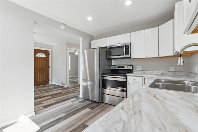 kitchen with stainless steel appliances, sink, light wood-type flooring, light stone countertops, and white cabinetry