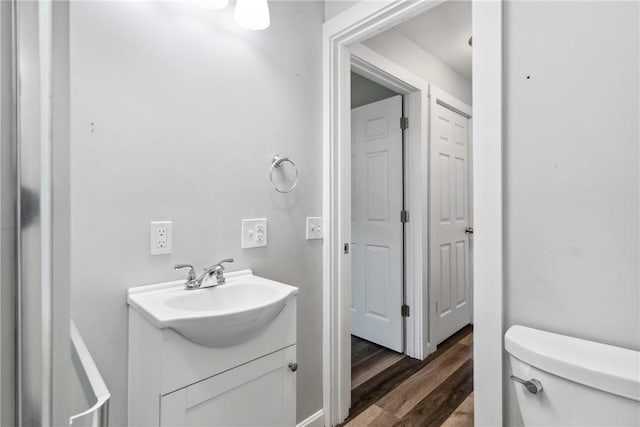 half bath with toilet, wood finished floors, and vanity