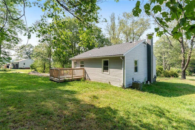 rear view of house featuring central AC unit, a chimney, a wooden deck, and a lawn