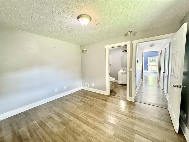 unfurnished bedroom featuring light wood-type flooring, connected bathroom, and a textured ceiling