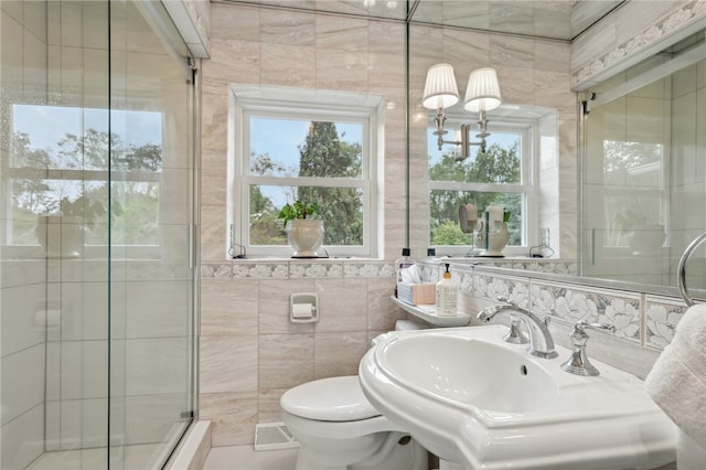 bathroom with tile walls, a shower with shower door, toilet, and a wealth of natural light