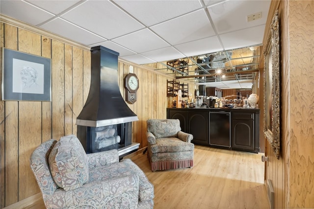 sitting room with light hardwood / wood-style floors, a drop ceiling, and wood walls