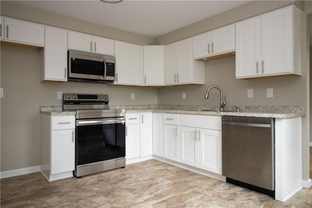 kitchen featuring a sink, light stone counters, white cabinetry, appliances with stainless steel finishes, and baseboards