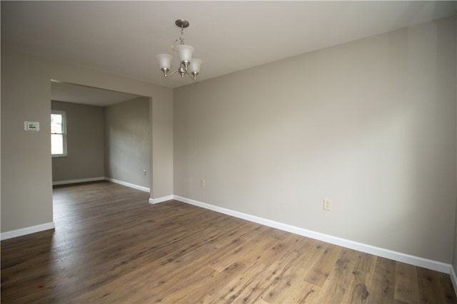 spare room with a chandelier, baseboards, and dark wood-style flooring