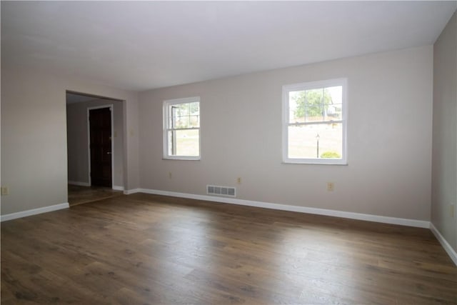 spare room with dark wood finished floors, visible vents, and baseboards