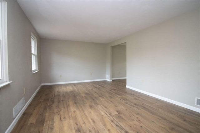 empty room featuring wood finished floors, visible vents, and baseboards