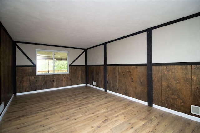 spare room with visible vents, wainscoting, wood walls, and wood finished floors