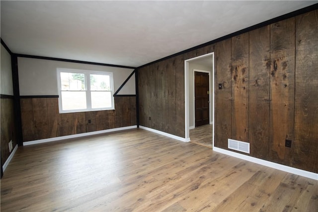 empty room with visible vents, wooden walls, wood finished floors, and crown molding