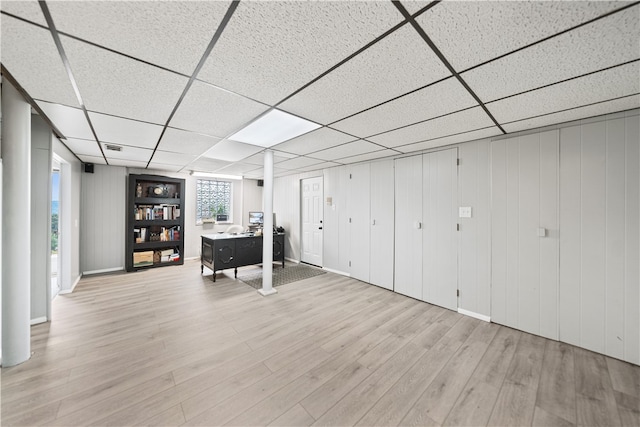 basement with a paneled ceiling, wood walls, and light hardwood / wood-style flooring