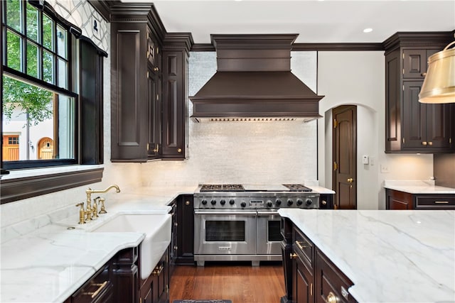 kitchen featuring dark hardwood / wood-style flooring, light stone countertops, custom exhaust hood, range with two ovens, and decorative backsplash