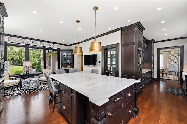 kitchen with a breakfast bar, a center island, light stone counters, dark hardwood / wood-style floors, and pendant lighting