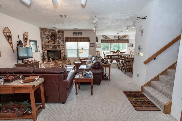 carpeted living room featuring a textured ceiling, an inviting chandelier, and a stone fireplace