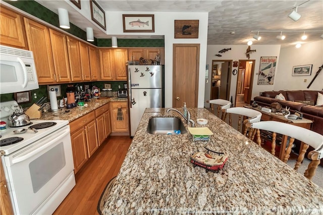 kitchen with white appliances, a center island with sink, sink, light stone countertops, and light hardwood / wood-style floors