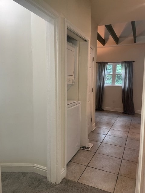 hallway with stacked washer / drying machine, beamed ceiling, and light tile patterned floors