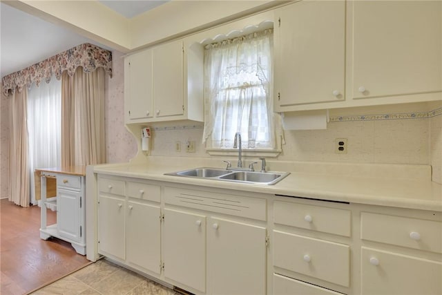 kitchen with a sink, white cabinetry, backsplash, and light countertops