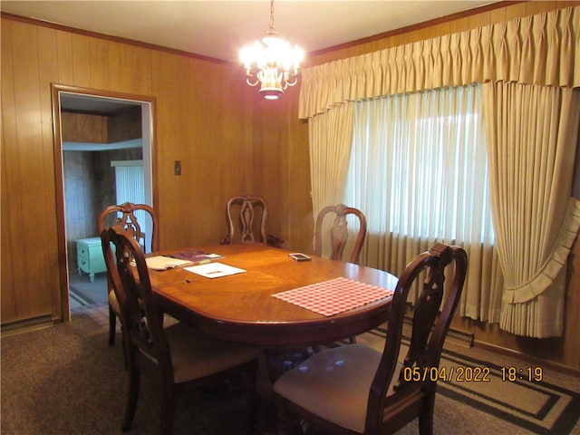 carpeted dining space with crown molding, a chandelier, and wooden walls