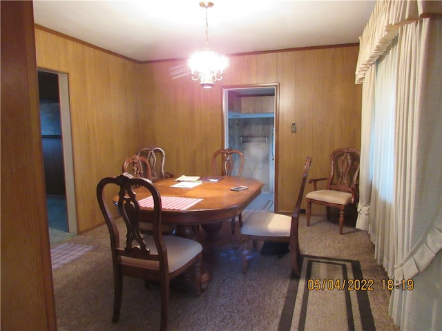 carpeted dining space featuring wood walls and a chandelier