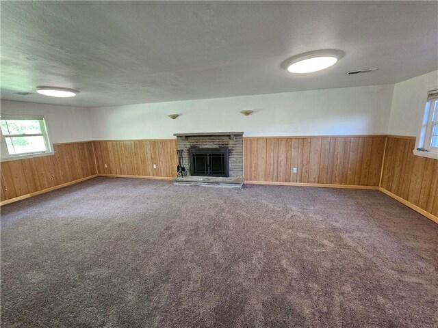 unfurnished living room featuring a textured ceiling, wooden walls, and dark carpet