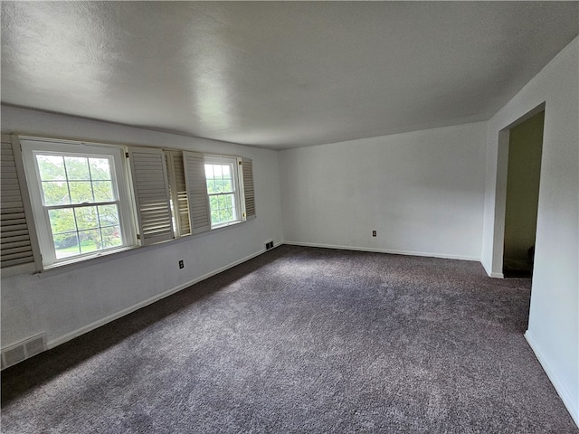 unfurnished room featuring dark colored carpet, a textured ceiling, and plenty of natural light