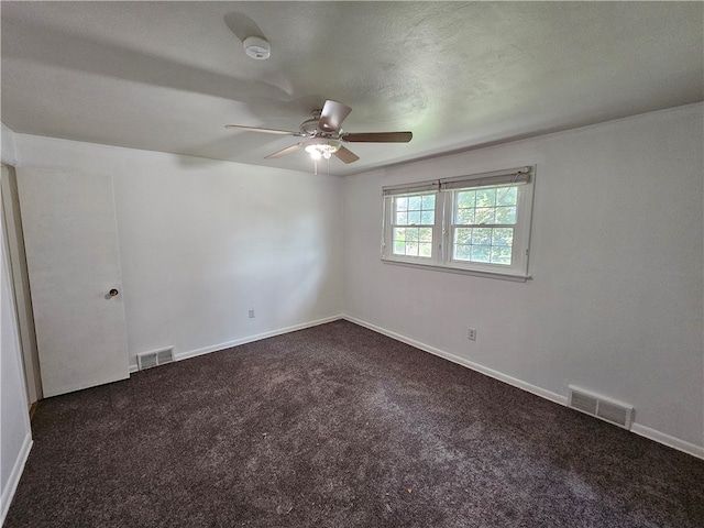 empty room featuring a textured ceiling, dark carpet, and ceiling fan