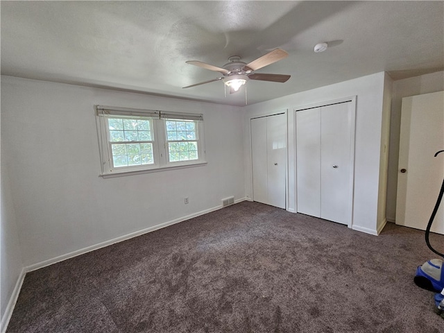 unfurnished bedroom with ceiling fan, dark colored carpet, a textured ceiling, and two closets