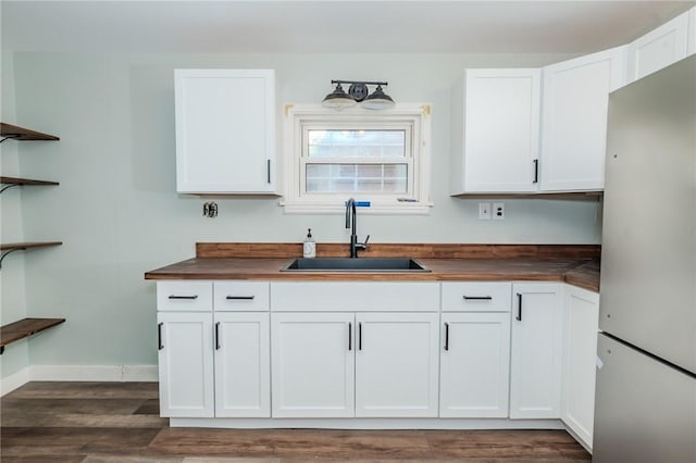 kitchen with stainless steel refrigerator, wood counters, sink, and white cabinets