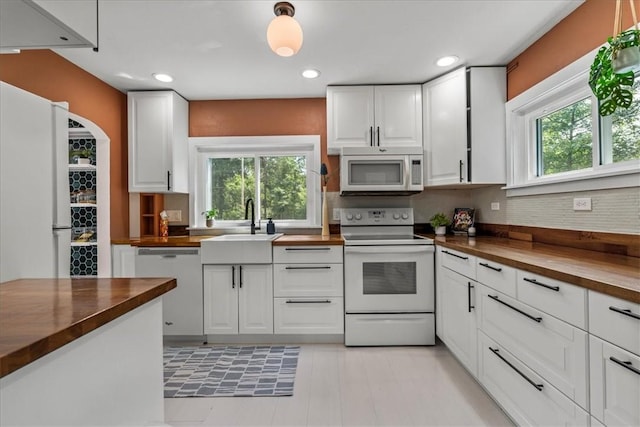 kitchen with wood counters, tasteful backsplash, sink, white cabinets, and white appliances