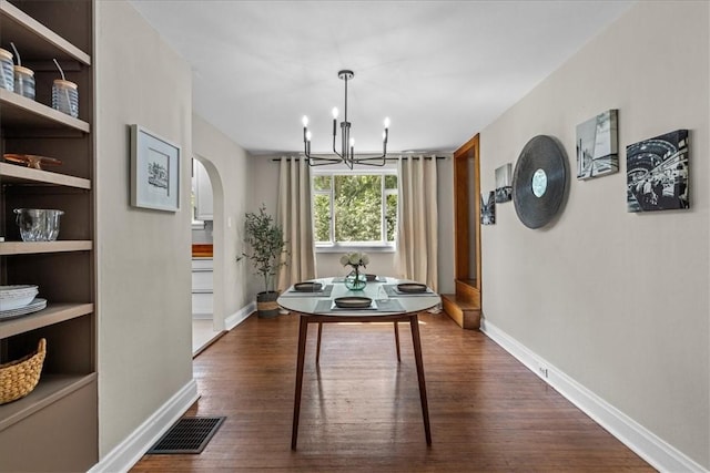 dining area with dark wood-type flooring and an inviting chandelier