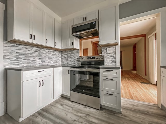 kitchen featuring white cabinets, range hood, light hardwood / wood-style floors, appliances with stainless steel finishes, and decorative backsplash