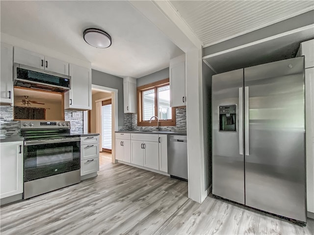 kitchen with appliances with stainless steel finishes, light wood-type flooring, tasteful backsplash, and white cabinets