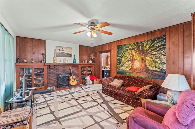 living room featuring wood walls, a wood stove, a brick fireplace, and ceiling fan