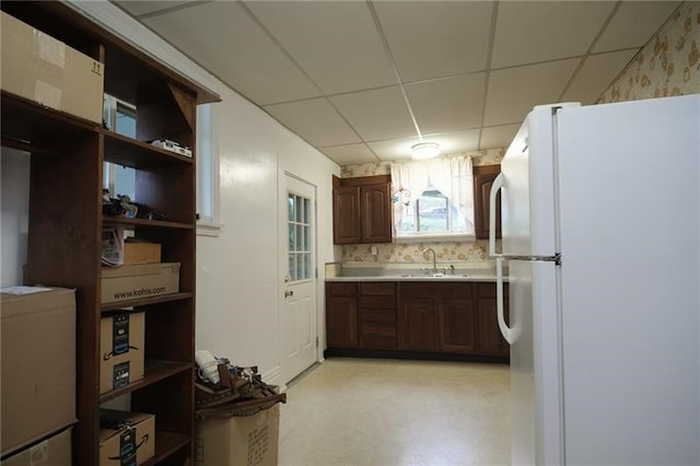 kitchen featuring white refrigerator, sink, dark brown cabinets, decorative backsplash, and a drop ceiling