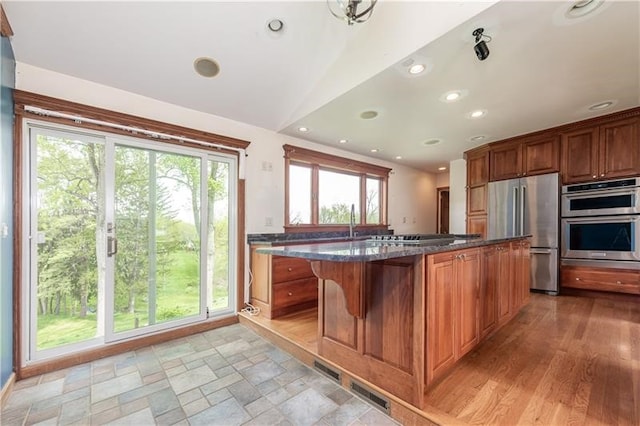 kitchen featuring light hardwood / wood-style flooring, a wealth of natural light, dark stone counters, stainless steel appliances, and a kitchen bar