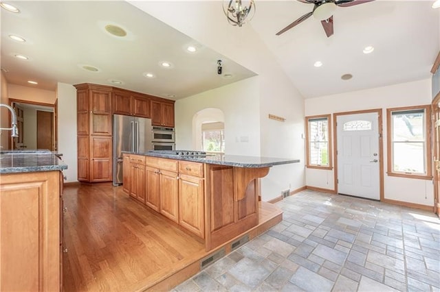 kitchen featuring ceiling fan, stainless steel appliances, a kitchen bar, light hardwood / wood-style flooring, and lofted ceiling