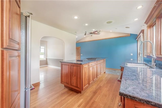 kitchen featuring dark stone countertops, light wood-type flooring, a kitchen island, vaulted ceiling, and sink