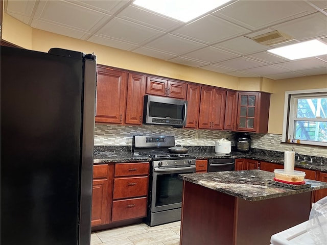 kitchen with light tile patterned floors, backsplash, black appliances, and dark stone countertops