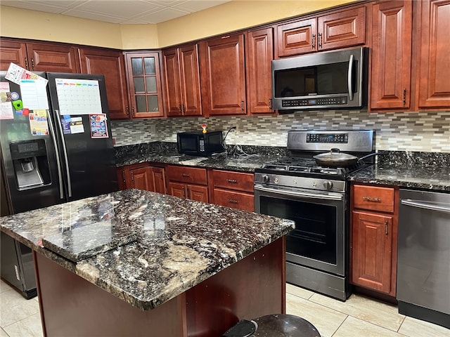 kitchen with black appliances, tasteful backsplash, dark stone countertops, a kitchen island, and light tile patterned floors