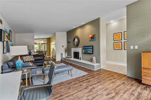 living room featuring an inviting chandelier, light wood-type flooring, and a brick fireplace