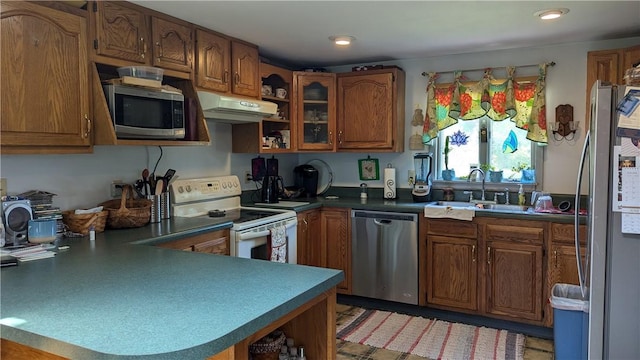 kitchen with brown cabinetry, a peninsula, stainless steel appliances, under cabinet range hood, and a sink