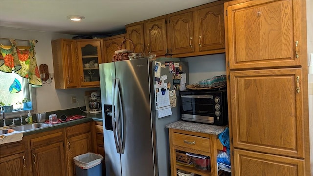 kitchen featuring dark countertops, glass insert cabinets, brown cabinetry, and stainless steel fridge with ice dispenser