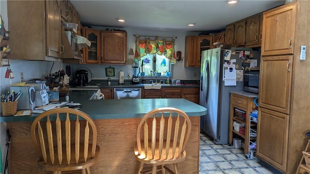 kitchen with dark countertops, glass insert cabinets, brown cabinetry, appliances with stainless steel finishes, and a sink