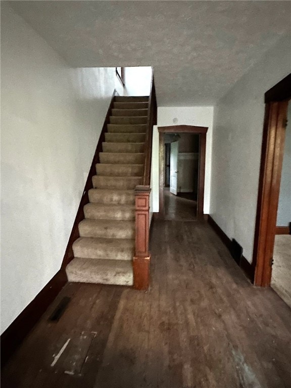 stairway with a textured ceiling and dark hardwood / wood-style flooring