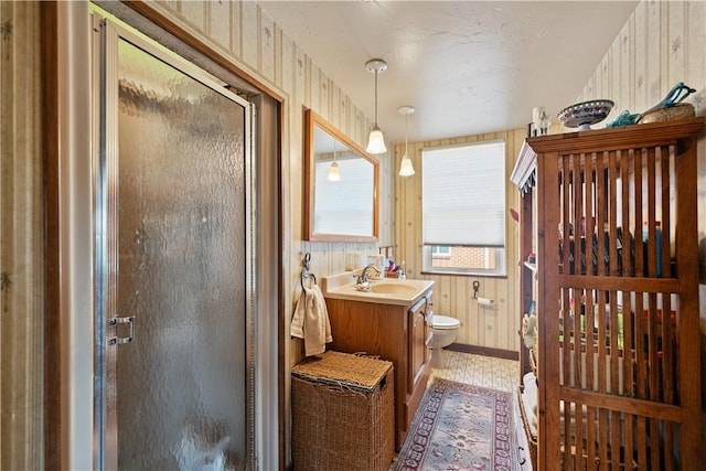 bathroom featuring wooden walls, toilet, a shower stall, and vanity